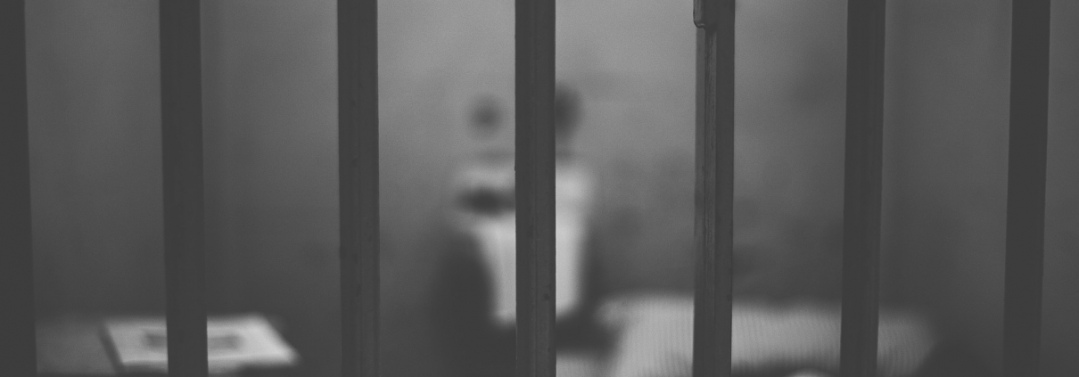 Imagen decorativa. Se observa una persona en la celda de una cárcel.
